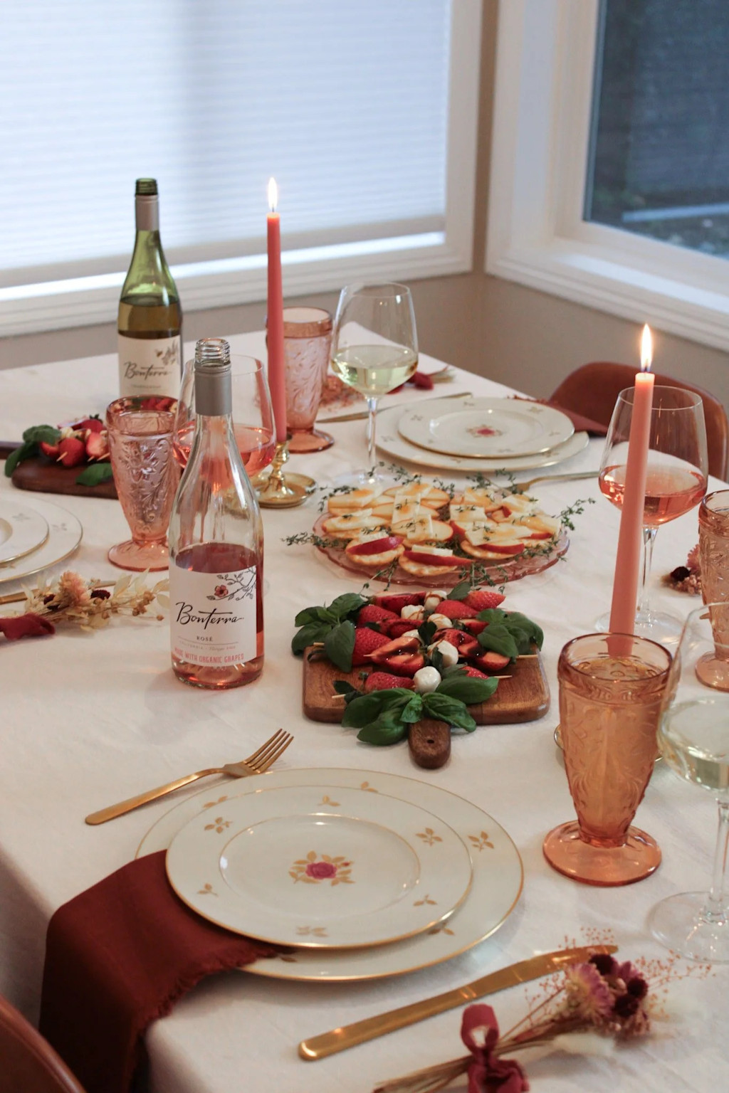 Romantic dining table set with rosé and white wine, appetizers, and lit candles for an enjoyable married couples party