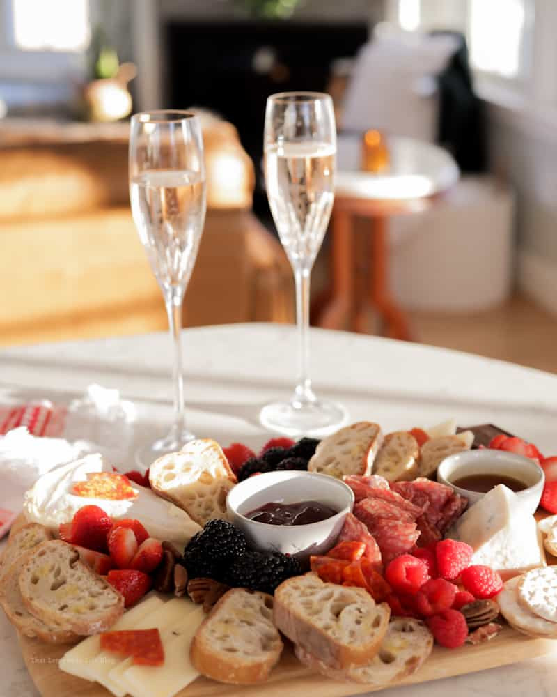 Wine and cheese charcuterie board for two with fresh fruits, nuts, and champagne glasses, ideal for intimate couples' celebrations